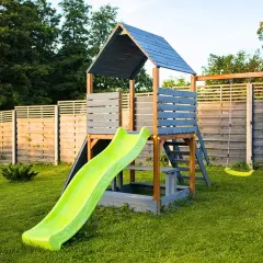 Drewniany domek dla dzieci ze zjeżdżalnią i huśtawkami. Idealne miejsce do zabawy na świeżym powietrzu, inspiracja, jak zrobić domek dla dzieci.