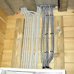 Instalacja elektryczna w domku drewnianym: wiązki kabli w szarych i metalowych peszlach wychodzące spod sufitu.