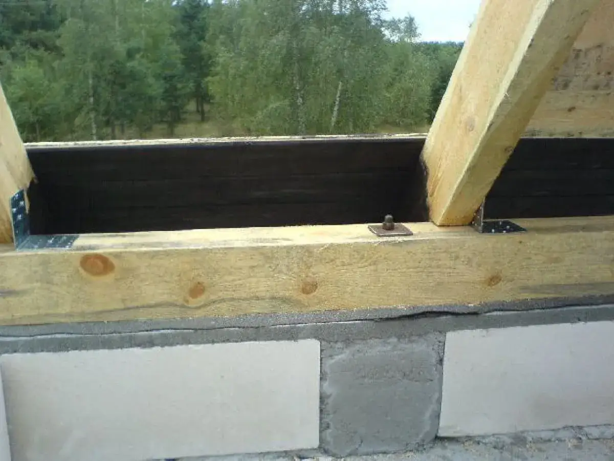 Drewniana belka na bloczkach betonowych, mocowanie murłaty bez wieńca. Metalowe kątowniki i śruba mocująca konstrukcję dachu.